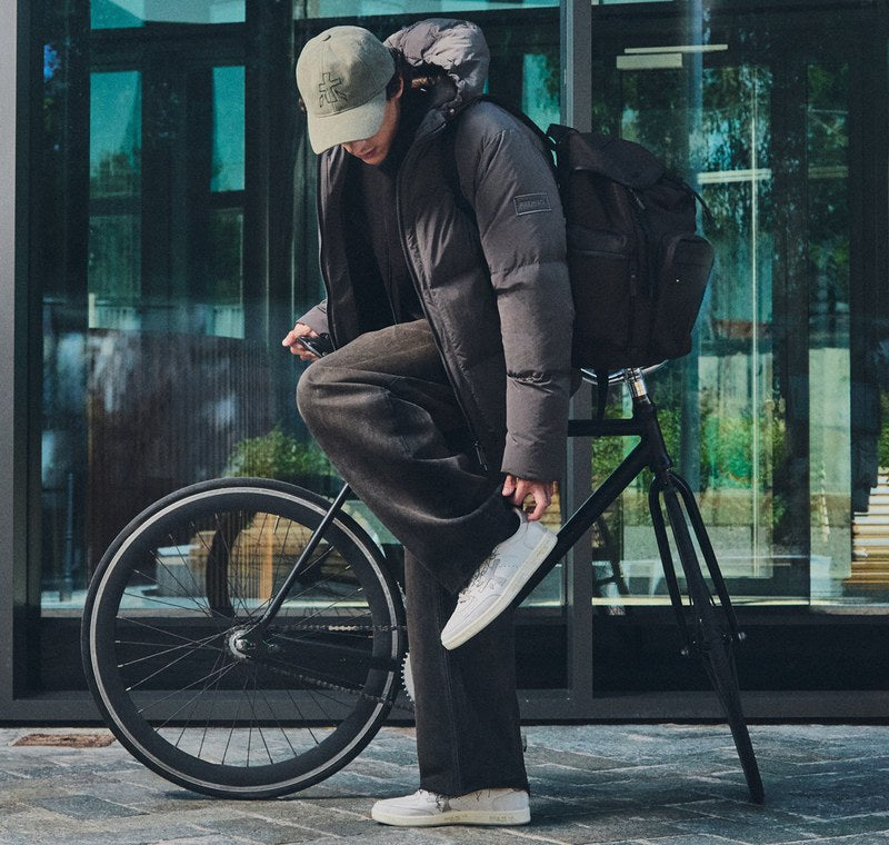 Uomo in bicicletta con sneaker Premiata bianche e dettaglio della sneaker sul pedale. Foto @premiataofficial
